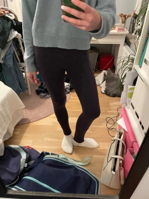 Svarta leggings i stretchigt material - Säljer ett par svarta leggings med tight passform. De är tillverkade i ett stretchigt syntetmaterial som sitter skönt mot kroppen. Perfekta för dig som gillar en enkel och stilren look. Passar till både oversized tröjor och hoodies.