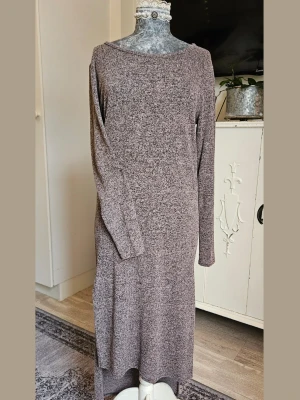 Lång stickad klänning i grått - Mysig lång stickad klänning i melerad grå ton med rund hals och långa ärmar. Klänningen har en rak passform och en slits. 