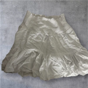 Vit volangkjol från 157 - Supersöt vit kortkjol från 157 med bred smock i midjan och volangig nederdel. Kjolen har en luftig känsla och är perfekt för varma dagar. Tillverkad i mjukt material som ger en skön passform och snygg siluett. ALDRIG ANVÄND 