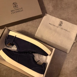 Mörkblå sneakers från Brunello Cucinelli - Snygga mörkblå sneakers från Brunello Cucinelli med ovandel i lyxig mocka och beige skinnfoder. Skorna har platt vit sula och klassisk snörning. Perfekt för dig som gillar stilrena och exklusiva detaljer. Made in Italy. Ny pris från 7000-11000, släpper för bra pris vid snabb affär 