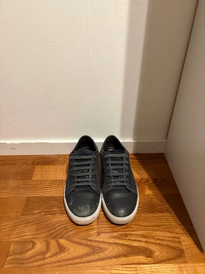Lanvin Paris - Snygga svarta sneakers med vit platt sula och rund tå. Ovandelen är i mocka med detaljer i skinn och har klassisk snörning. Perfekt för dig som gillar stilrena och enkla skor med en modern touch.