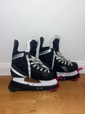 Barn storlek 36 hockeyskridskor - Säljer ett par svarta Pulse 4 hockeyskridskor med vita detaljer och snörning. Skridskorna har en robust design med vit och silverfärgad kant, samt mjuk vit vaddering på insidan för extra komfort. Storlek 36