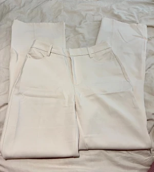 Beige kostymbyxor  - Snygga beige kostymbyxor med Byxorna har bälteshällor och är tillverkade i ett slätt material som ger en stilren look. Perfekta för dig som gillar minimalistisk och clean stil.