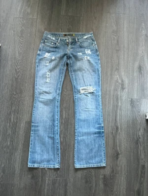 Blå bootcut jeans  - Säljer ett par blå jeans med bootcut passform och slitna detaljer framtill.  