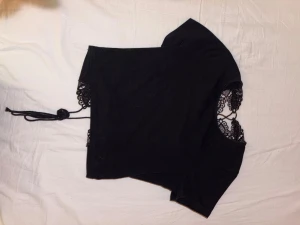 Svart korsett-topp med spets och snörning - Säljer en svart korsett-topp med korta ärmar och snygga spetsdetaljer framtill och vid axlarna. Toppen har snörning i midjan som ger en cool look och croppad passform. Perfekt för dig som gillar att sticka ut med detaljer och svart vibe.