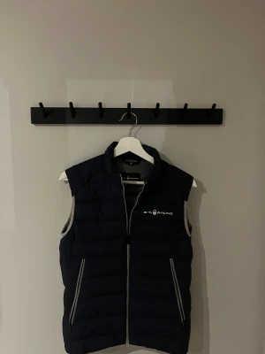 Mörkblå dunväst från Sail Racing - Väst från Sail Racing i mörkblå färg med grå insida och detaljer. Säljer västen för att den har blivit för liten. Men den är i mycket bra skick. Storlek xs