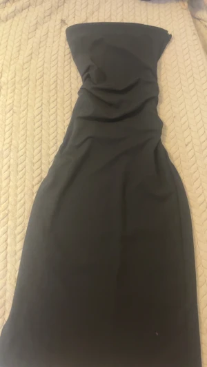 Svart axelbandslös långklänning - Säljer en elegant svart axelbandslös långklänning med figurnära passform. Klänningen har en stilren och enkel design utan mönster, perfekt för dig som gillar minimalistisk stil. Materialet känns mjukt och följsamt mot kroppen.