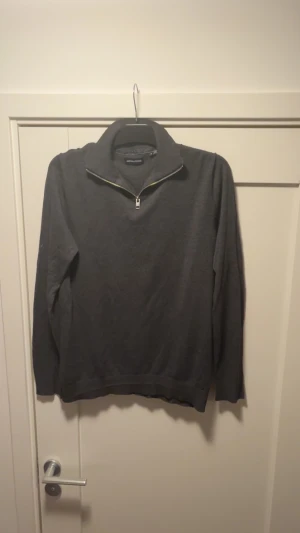 Mörkgrå half quarter tröja Jack & Jones - Snygg mörkgrå långärmad tröja från Jack & Jones med krage och half zip-dragkedja framtill. Perfekt för dig som gillar stilrena och enkla plagg. Materialet är mjukt och känns skönt mot huden. Passar dig som vill ha en klassisk look med modern touch.