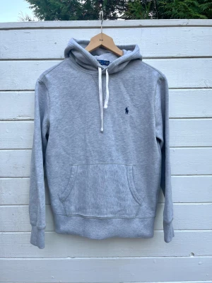 Ralph Lauren Grå Hoodie  - Supersnygg grå Ralph Lauren Hoodie. Storlek S, passar som en tajtare S eller som en XS. I ett fint skick, skön att använda. Finns en liten defekt (minimal fläck) på sista bilden men den är på undersidan av ena armen så syns inte i verkligheten speciellt mycket. Kan säkert gå bort i tvätt, har inte provat ännu. Perfekt julklapp☃️