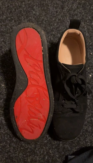 Svarta Christian Louboutin sneakers - Svarta sneakers från Christian Louboutin med klassisk röd sula och signaturlogga. Skorna har rund tå, snörning och är tillverkade i mocka med skinnfoder. Snygg och stilren design som sticker ut med den röda undersidan.