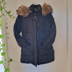 Hollies Wilma dunjacka - Svart Wilma från Holliies, stoppad med dun och med supermjuk, fluffig fauxpäls i kragen. Stor huva, dragkedja samt knappar, 5 fickor fram. Använd fåtal gånger, så som ny 🤗