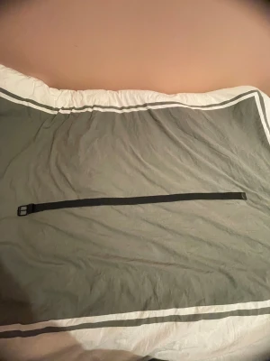 Svart Urban Classics bälte - Snyggt svart bälte från Urban Classics med flätad design och detaljer i konstläder. Spännet är i svart metall och bältet har en stilren look som passar till jeans eller kostymbyxor. Perfekt accessoar för att lyfta din outfit.