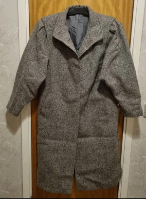 Grå rutig kappa med klassisk krage - Snygg grå kappa med diskret rutig mönster och klassisk krage. Jackan har lång ärm och två fickor framtill. Perfekt för dig som gillar stilrena och tidlösa plagg med lite oversized känsla. Kappa av 100%ull, kan passa som L/Xl