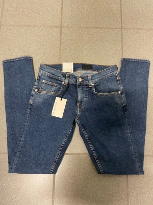 Blå Tiger of Sweden jeans W29 L32 - Snygga blå jeans från Tiger of Sweden med klassisk femficksdesign, smal passform och smala ben. Jeansen har orange kontrastsömmar, läderpatch bak och är tillverkade i slitstarkt denim. Perfekta för dig som gillar en stilren och modern look.