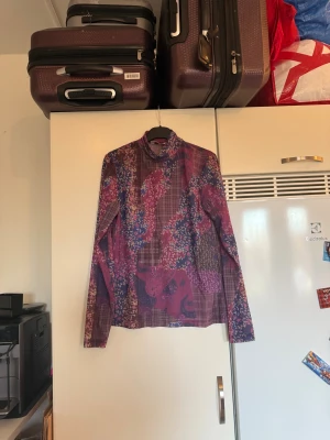 Mönstrad polotopp från Odd Molly - Säljer en färgstark polotopp från Odd Molly med lång ärm. Toppen har ett unikt patchworkmönster med blommiga och rutiga inslag i lila, vinrött, blått och rosa toner. Materialet är lätt och känns skönt mot huden. Perfekt för dig som gillar statement-plagg! Storlek 4 som enligt deras storleksguide motsvarar en stoelwk XL. Men den ör något liten i storlek. Mycket fint skick, jag hittar inga synliga anmärkningar eller defekter. 