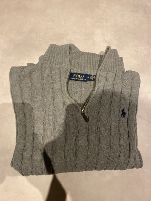 Grå stickad knitwear half zip tröja från Ralph Lauren - Säljer denna jätte snygga kabelstickade half zipen från Ralph lauren. Den är i storlek m och modellen är 183cm,74 kg. Tröjan är knappast använd och har jätte bra passform. Inga hål eller defekter alls!