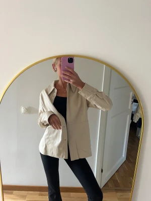 Beige overshirt i skinnimitation - Snygg beige overshirt med klassisk krage & knappar hela vägen framtill. Jackan har långa ärmar med knappdetalj vid mudden & är gjord i mjuk skinnimitation. Superfint skick & endast använd någon gång. Är ifrån Gina tricot & i storlek XS. Säljer då den tyvärr inte kommer till användning av mig🤎