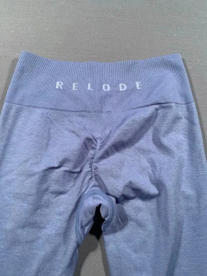 Ljusblå leggings från Relode - Säljer ett par ljusblå leggings från Relode med hög midja och bred resår. De är tighta och stretchiga, perfekta för träning eller chill. Materialet känns mjukt och följsamt mot kroppen. Diskret logga framtill i midjan.