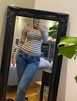 Randig offshoulder topp i bomull - Säljer en vit och svart randig offshoulder topp med långa ärmar. Toppen är croppad och har en slim passform som sitter snyggt mot kroppen. Materialet är mjuk bomull och toppen har en cool, ungdomlig vibe. Perfekt för dig som gillar trendiga och bekväma plagg.