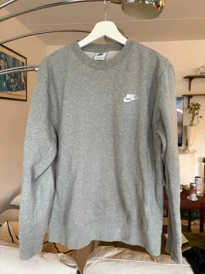 Grå sweatshirt från Nike i medium - Säljer en grå crewneck sweatshirt från Nike i storlek medium. Tröjan har klassisk rund hals, långärmade ärmar och ett litet vitt Nike-logotryck på bröstet. Mjuk insida i fleece och ribbade muddar vid ärmslut och nederkant. Perfekt för chill eller träning.