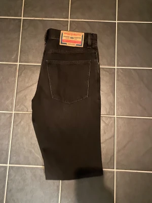 Svarta Diesel Larkee jeans straight fit - Svarta jeans från Diesel, modell Larkee, med klassisk straight fit och normal passform. Jeansen har fem fickor, bälteshällor och en snygg Diesel Industry-patch bak i midjan. Materialet är robust denim i bomull. Perfekt för dig som gillar stilrena och tidlösa jeans.