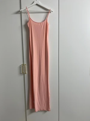 Ljusrosa långklänning med smala axelband - Säljer en enkel och stilren ljusrosa långklänning med smala axelband. Klänningen har en rak passform och ärmlös design, perfekt för varma dagar. Materialet känns mjukt och följsamt mot kroppen. Passar dig som gillar minimalistisk och fräsch stil.