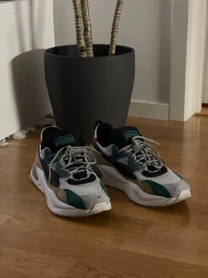 Puma x The Hundreds sneakers strl 45 - Feta Puma x The Hundreds sneakers i storlek 45. Skorna har en mix av mesh och mocka i vitt, svart, grönt, blått och beige med coola detaljer och tjock sula. Grå snörning och branding på både plös och häl. Perfekt för dig som gillar streetwear och unika samarbeten.