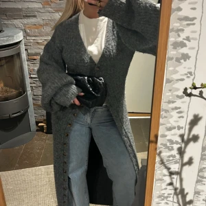 Stickad adooreklänning - Säljer denna ribbstickad lång klänningen/kofta i mörkgrått med v-ringad hals och stora ballongärmar från Adoore!. Har används en del, men väl behållen och utan defekter!