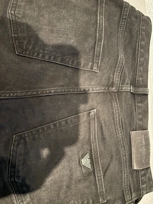 Svarta skinny jeans Emporio Armani - Snygga svarta skinny jeans från Emporio Armani med klassisk femficksdesign och ikoniska EA-loggan på bakfickan. Jeansen har smal passform, bälteshällor och metallknapp framtill. Tillverkade i stretchig bomullsblandning för skön känsla.