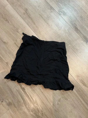 Svart volangkjol från SHEIN - Svart kortkjol från SHEIN i storlek S. Kjolen har en söt volangkant längst ner och en diskret dragkedja i sidan. Knappt använd.