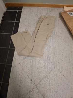 Beige chinos från Dondup, storlek 28 - Säljer ett par snygga beige chinos från Dondup, tillverkade i Italien. Byxorna har klassisk passform med bälteshällor, knapp och dragkedja framtill samt fickor bak. Perfekta för en clean och stilren look.