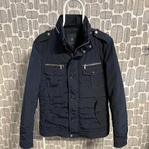 Mörkblå jacka från Riley - Snygg mörkblå jacka från Riley med dragkedja och knappar. Mycket bra skick, priset går att diskutera. Hör bara av dig vid någon fråga.