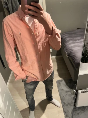 Rosa skjorta från Ralph Lauren - Snygg rosa skjorta från Ralph Lauren med klassisk button-down krage och broderad logga på bröstet. Skjortan har långa ärmar, knappar framtill och är gjord i mjuk bomull. Perfekt för dig som gillar stilrena och fräscha plagg med lite färg. Helt ny aldrig använd 