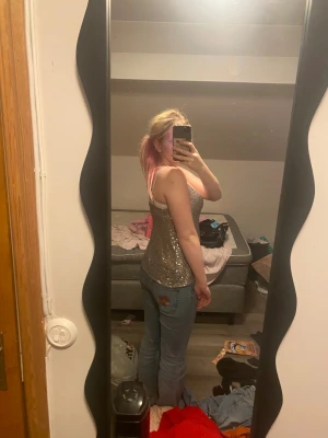 Glittrig silver linnetopp med paljetter - Storleken är XS men själv är jag Medium och den sitter perfekt. Säljer en snygg linnetopp i silver med tunna axelband och v-ringad front. Toppen är täckt av glittrande paljetter som ger en riktigt festlig vibe. Perfekt för dig som vill sticka ut och glänsa.