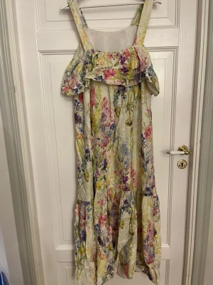 Blommig långklänning från H&M MAMA - Superfin långklänning från H&M MAMA med breda axelband och volang upptill. Klänningen har ett ljust blommigt mönster i rosa, lila, blått och gult på en vit/beige bas. Perfekt för sommarens alla tillfällen, med luftig passform och mjukt material.