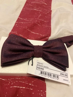 Mörkröd Andover fluga i siden - Snygg mörkröd fluga från Andover i färgen Tawny Port. Flugan har ett subtilt mönster och är tillverkad i siden, vilket ger en lyxig känsla och fin glans. Perfekt accessoar för att lyfta din outfit med lite extra stil. En väldigt unik och fin färg på flugan. Nypris är 299, jag säljer för 150kr. Den är använd i väldigt gott skick. 