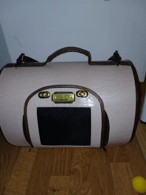 Hund burBeige och brun väska från Top Dog - Snygg beige och brun väska från Top Dog med krokopräglat mönster och detaljer i guld. Väskan har svart nät på sidorna och framtill, samt både handtag och axelrem. Perfekt för dig som vill resa med stil och ha allt organiserat.