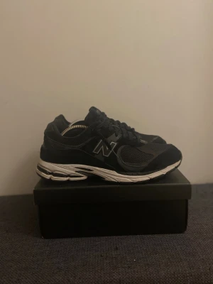 New balance 2002R - Säljer ett par svarta New Balance sneakers med mesh och mockadetaljer. Skorna har en chunky vit sula med svarta inslag och klassisk snörning. Ikoniskt N på sidan och rund tå. Perfekta för dig som gillar sportig och clean stil.