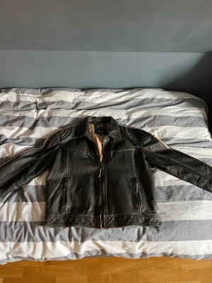 Svart skinnjacka från Molltan 3XL - Svart skinnjacka från Molltan i storlek 3XL. Jackan har coola quiltade detaljer på axlarna, dragkedjor framtill och på fickorna samt en klassisk krage. Snygga kontrastsömmar och beige foder ger extra stilpoäng. Perfekt för dig som gillar street och edgy vibe.