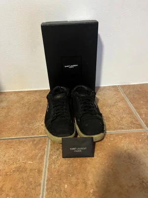  Saint Laurent skor - Svarta sneakers från Saint Laurent med broderad logga på sidan och beige sula. Skornar i relativt dåligt skick men har liv kvar att ge, dem behöver bara lite kärlek. Skorna är perfekt som julklapp eller om du söker ett par själv!                                             Priser går självklart att diskutera!Tveka inte på att skriva om du vill ha fler bilder eller om du har någon fråga🤝