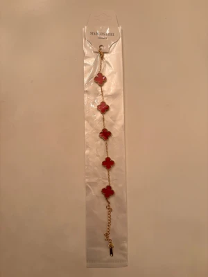 Van Cleef Armband - Snyggt armband i rostfritt stål med fem röda klöverformade länkar infattade i guldfärgad metall. Perfekt som present inför julafton. Skriv gärna för mer frågor.