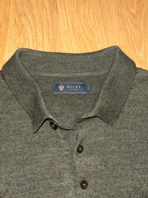 Grön stickad pikétröja från Riley - Snygg grön stickad pikétröja från Riley med klassisk krage och tre knappar framtill. Tröjan har långärmad design och är tillverkad i mjukt stickat material som känns skönt mot huden. Perfekt för dig som gillar stilrena och enkla plagg. Storleken är felaktig passar bättre på M