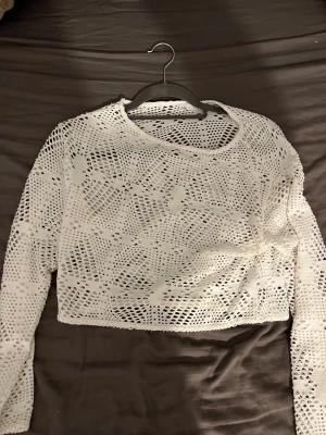Vit virkad croppad topp från lager  157 - Säljer en vit croppad topp från lager  157 i storlek XS. Toppen är virkad med ett snyggt hålmönster och har långa ärmar. Perfekt för dig som gillar boho-vibe och vill ha något luftigt och coolt. Rund halsringning och mjukt material som känns skönt mot huden.
