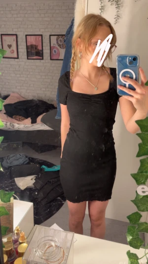 Svart kort klänning - Svart kort klänning från H&M med fyrkantig ringning och scrunch framtill. Klänningen har korta ärmar och lätt vågig kant nertill. Mjuk och stretchig i materialet, perfekt för en enkel och stilren look.