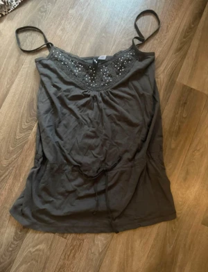 Grå linnetopp med glitter, strl 34 - Grå linnetopp med smala axelband och snyggt glitter på upptill. Dekorativ spets runt halsringningen och knytband i midjan för extra passform. Super snygg💕