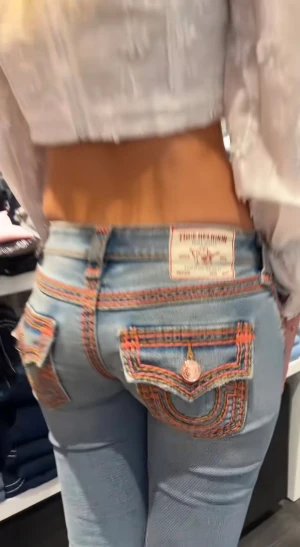 True Religion jeans med orange detaljer - Säljer ett par ljusblå True Religion jeans med orange och röda kontrastsömmar, ikoniska ficklock med knapp och dekorativa detaljer längs benen. Modellen har låg midja och bootcut passform. Jeansen är tillverkade i klassiskt denimtyg och har unika broderade fickor. De var löppta för 2300kr och säljs för billigare 