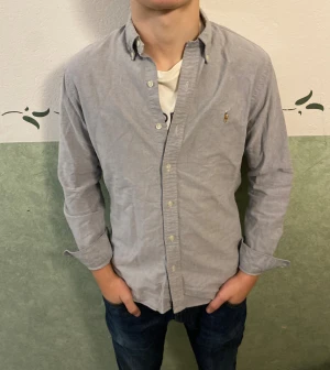 Ljusblå skjorta från Polo Ralph Lauren - Säljer en stilren ljusblå skjorta från Polo Ralph Lauren i slim fit. Skjortan har klassisk button-down krage, långa ärmar och små vita knappar framtill. Broderad logga på bröstet. Perfekt för dig som gillar en clean och tidlös look.