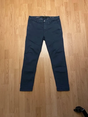 Replay chinos - Snygga marinblå Replay Hyperflex Zeumar byxor med slim passform. Byxorna har klassiska fickor fram och bak, bälteshällor och stängs med knapp och dragkedja. Stretchigt material för extra komfort och rörelsefrihet.