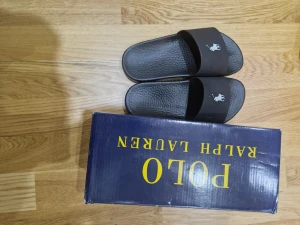 Svarta sandaler från Polo Ralph Lauren - Svarta sandaler från Polo Ralph Lauren med klassisk slide-design. De har en bred rem med Polo-logga i vitt och en strukturerad sula för extra grepp. Perfekta för sommaren och chill dagar. Materialet är syntet och de kommer i originalkartong. Kom med pris förslag
