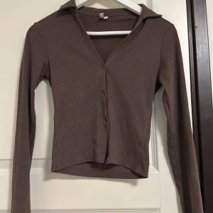 Brun ribbad kofta från Ivy Trend - Säljer en brun ribbad kofta från Ivy Trend i storlek XS. Koftan har v-ringning, krage och knappar. Långärmad och i stretchigt material som sitter snyggt på kroppen. Perfekt att styla med jeans eller kjol.